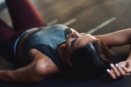 Young exhausted caucasian woman in sportswear lying on the floor at gym and resting after workout, taking a break. Sport, training, wellness and healthy lifestyle