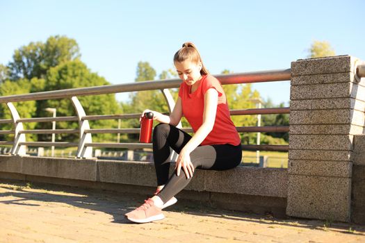 Attractive young woman in sports clothing taking a break while sitting outdoors