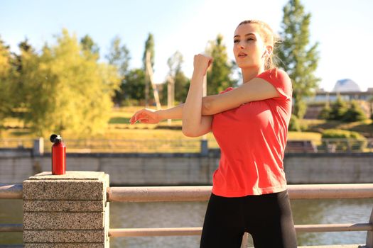 Beautiful young woman in sports clothing stretching her arms and looking concentrated while standing on the bridge