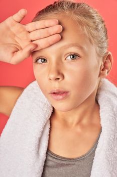 Close up of cute girl with towel around her neck touching forehead and looking at camera with serious expression