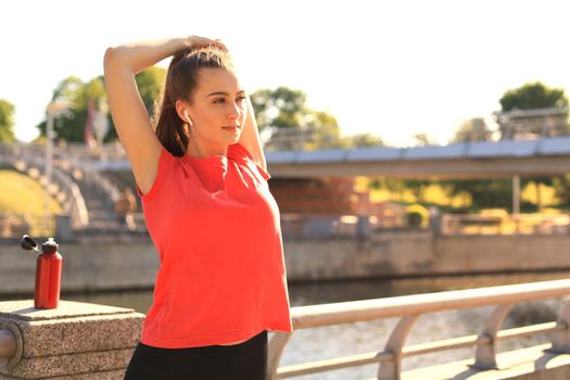 Beautiful young woman in sports clothing stretching her arms and looking concentrated while standing on the bridge