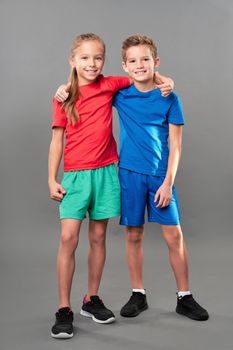 Cute female child wrapping arm around brother shoulder and smiling while standing against gray background