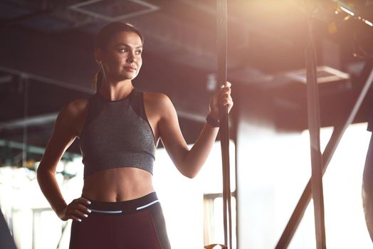 Young attractive sportive woman wearing sportswear looking away while standing at gym. Sport, workout, wellness and healthy lifestyle