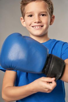 Adorable male child boxer looking at camera and smiling while tightening boxing glove around wrist before practice