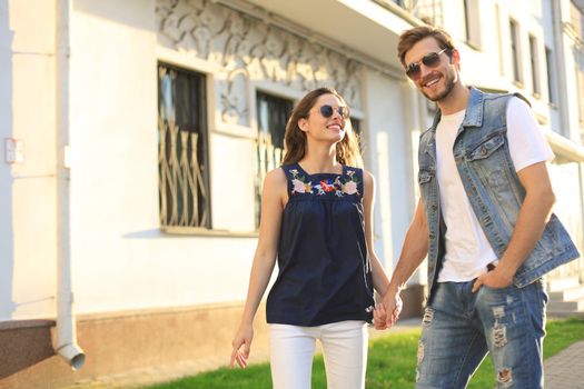 Image of lovely happy couple in summer clothes smiling and holding hands together while walking through city street