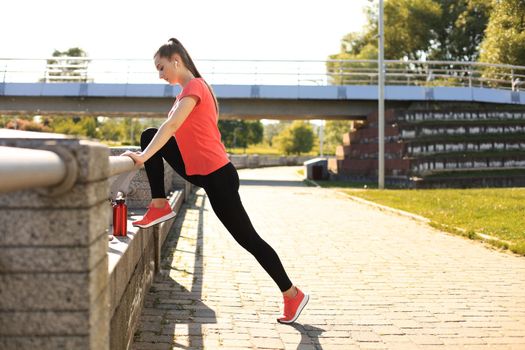 Beautiful young woman in sports clothing stretching while standing outdoors