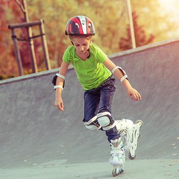 Little girl on roller skates in helmet at a park at sunset