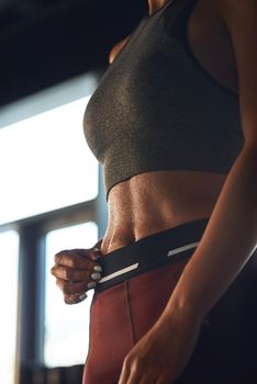 Vertical shot of athletic fitness woman wearing sports clothes showing perfect abs while working out at gym. Sport, training and healthy lifestyle
