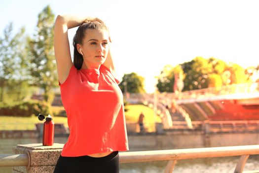 Beautiful young woman in sports clothing stretching her arms and looking concentrated while standing on the bridge