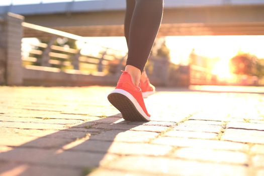 Close up of young woman in sports shoes jogging while exercising outdoors