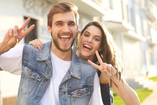 Image of a happy smiling cheerful young couple outdoors take a selfie by camera showing peace