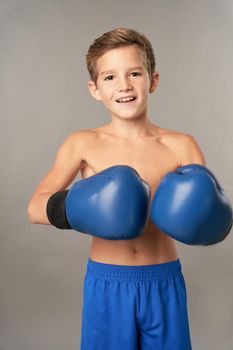 Cheerful male child boxer wearing boxing gloves and shorts while looking at camera and smiling