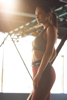 Building the ideal body. Vertical shot of young beautiful athletic woman wearing sports clothes looking away while standing at gym, resting after workout. Sport, training and healthy lifestyle