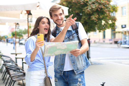 Beautiful young couple holding a map and smiling while standing outdoors