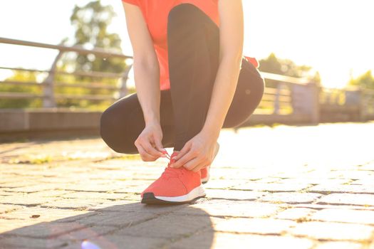 Closeup of unrecognizable sport woman tying sports shoes during evening run outdoors