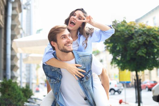 Handsome young man carrying young attractive woman on shoulders while spending time together outdoors