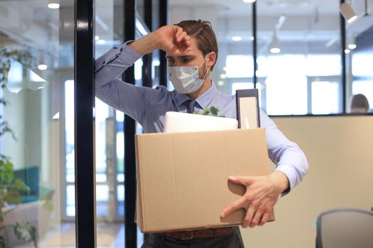 Dismissal employee in preventive medical mask in an epidemic coronavirus. Dismissed worker going from the office with his office supplies