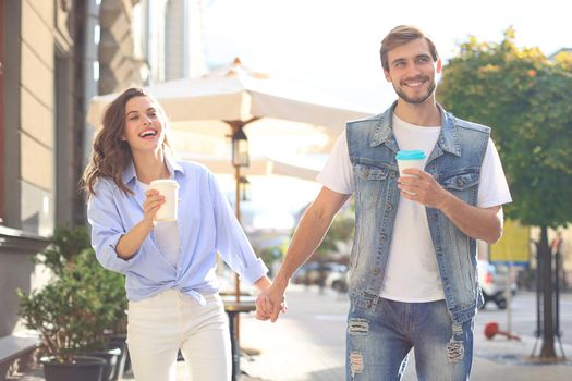 Image of lovely happy couple in summer clothes smiling and holding hands together while walking through city street