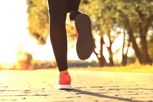 Close up of young woman in sports shoes jogging while exercising outdoors