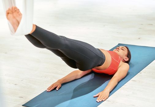 Young sportive woman lying on yoga mat in studio and doing sport exercises, practicing fly yoga. Wellness and healthy lifestyle