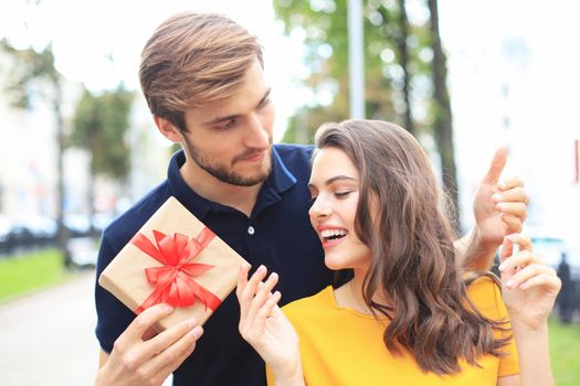 Image of charming excited couple in summer clothes smiling and holding present box outdoor