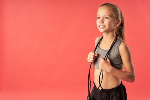 Cheerful cute girl in sportswear looking away and smiling while holding jump rope