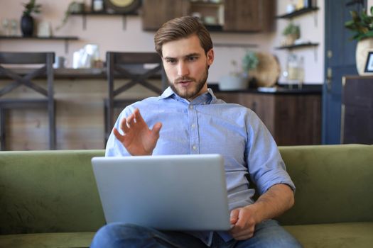 Smiling businessman greeting colleagues in video conference and negotiating distantly from home