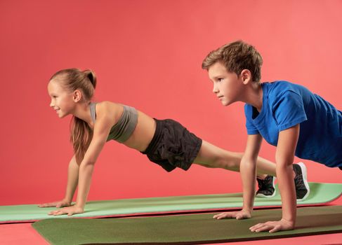 Cute kids in sportswear holding push-up position while doing strength exercise and using yoga mats