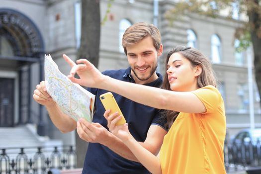 Beautiful young couple holding a map and smiling while standing outdoors