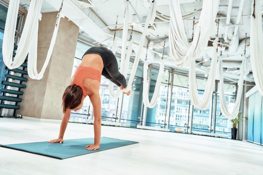 Bring harmony to your body. Young sporty woman practicing fly or aerial yoga, exercising with a hammock in studio, full length. Sport, wellness and healthy lifestyle