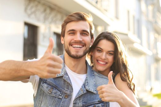 Image of a happy smiling cheerful young couple outdoors take a selfie by camera showing thumbs up