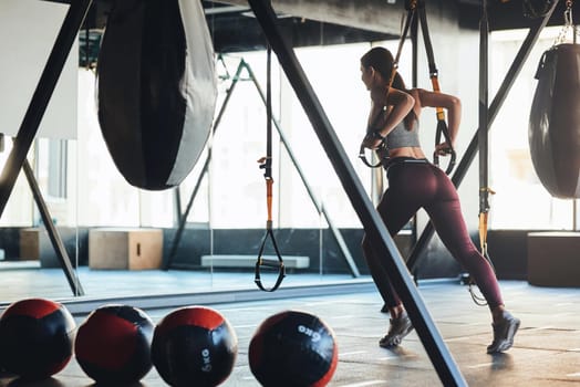 Young athletic woman with beautiful body wearing sports clothes exercising with fitness trx straps at gym. Sport, workout, wellness and healthy lifestyle