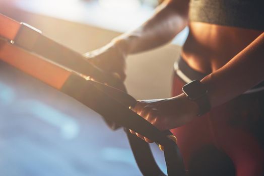 Close up shot of a woman exercising with fitness trx straps at gym, focus on female hand. Sport, workout, wellness and healthy lifestyle