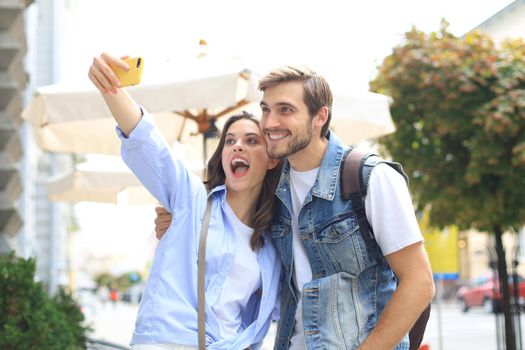 Beautiful lovely young couple walking at the city streets, hugging while taking a selfie