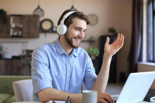 Happy young man in earphones working on laptop from home during self isolation