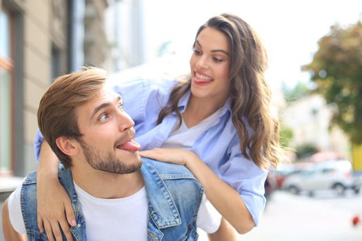 Handsome young man carrying young attractive woman on shoulders while spending time together outdoors