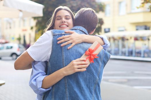 Image of attractive woman with present box giving hug to her man