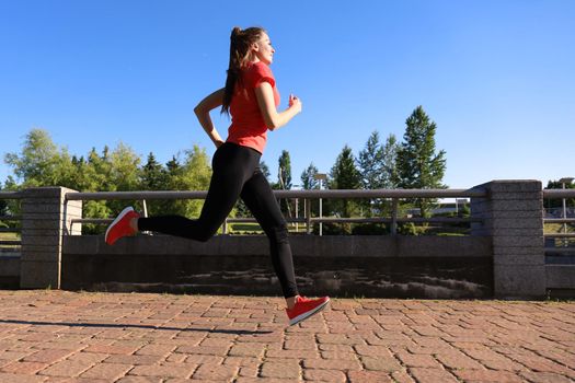 Photo of modern young woman in sports clothing jumping while exercising outdoors