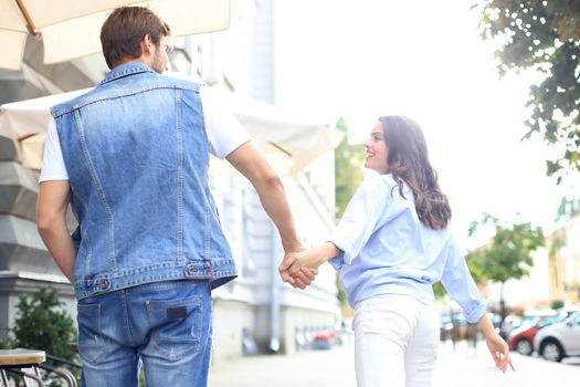 Rear view of beautiful young couple holding hands while walking through the city street