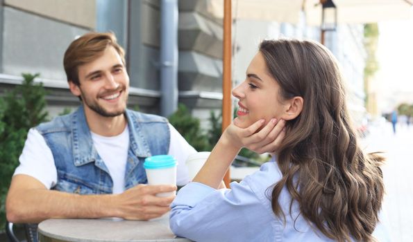 Attractive young couple in love drinking coffee while sitting at the cafe table outdoors