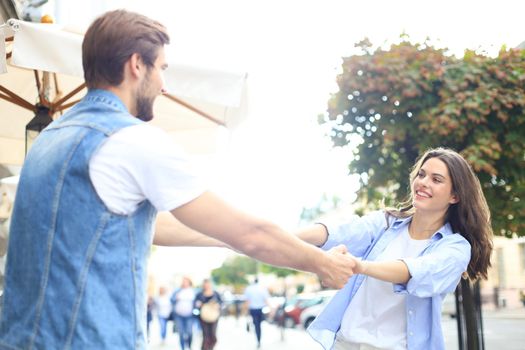 Beautiful young couple holding hands and spinning while standing on the city street