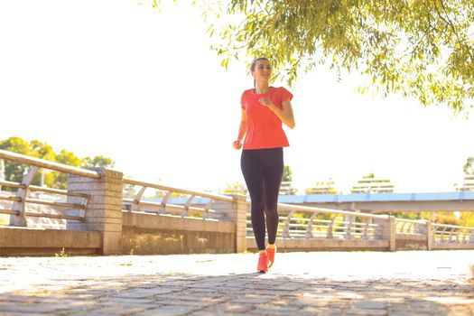 Beautiful young woman in sports clothing running while exercising outdoors