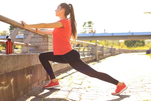 Attractive young fitness woman wearing sports clothing exercising outdoors, stretching exercises