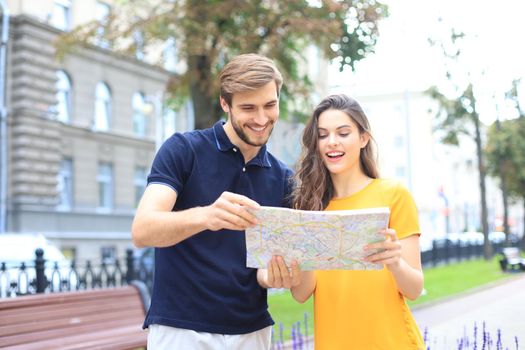 Beautiful young couple holding a map and smiling while standing outdoors