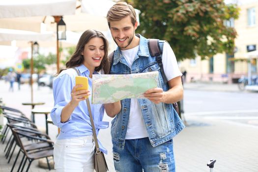 Beautiful young couple holding a map and smiling while standing outdoors