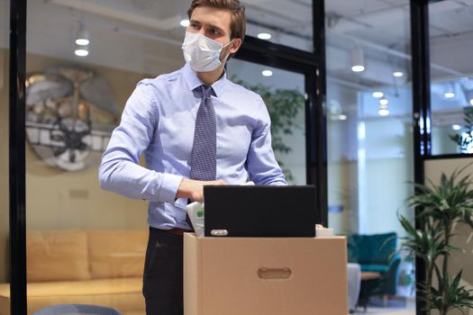Dismissal employee in preventive medical mask in an epidemic coronavirus. Sad dismissed worker are taking his office supplies with him from office