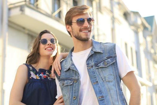 Image of lovely happy couple in summer clothes smiling and holding hands together while walking through city street