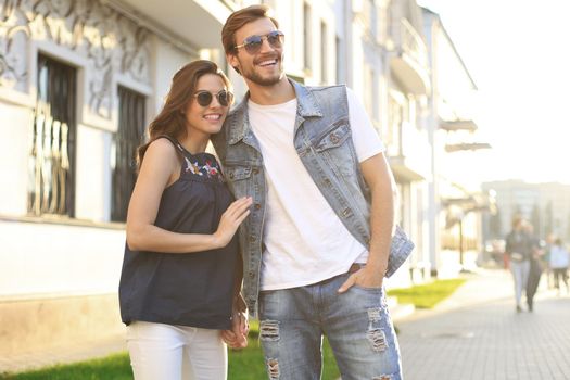 Image of lovely happy couple in summer clothes smiling and holding hands together while walking through city street