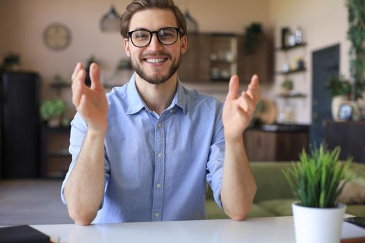 Confident happy businessman in eyeglasses sitting at home workplace and looking at camera