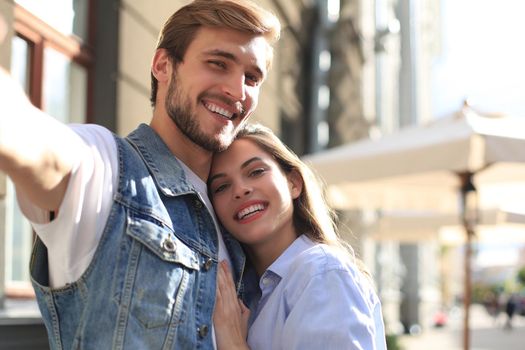 Beautiful lovely young couple walking at the city streets, hugging while taking a selfie